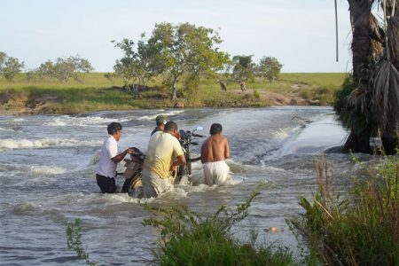 Not bikers fest: Heavy rains in the South Rupununi a few weeks ago saw creeks and streams overflowing their banks and bridges being covered leaving travelers stranded unless they decided to lift their motorbikes over the raging waters as in this case on the road heading to Karaudarnau. 