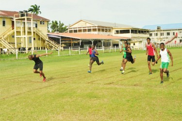 Tevin Garraway (first right) grimaces in pain a few metres from the finish line as Kevin Abbensetts forges ahead during the boys 100m IGG trials held last week. 