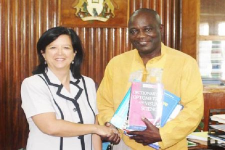 UG Vice Chancellor Prof Jacob Opadeyi and Dr Michele Ming shake hands as he displays some of the books donated to the university.
