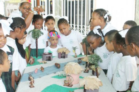 Mae’s students viewing a miniature Amerindian village at an exhibition held at the school in observance of Amerindian Heritage Month yesterday. (Photo by Arian Browne)
