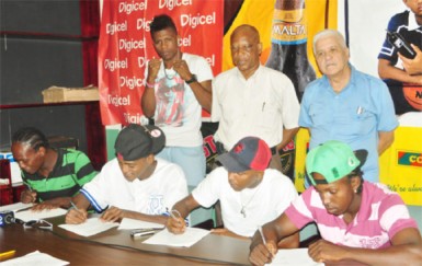 Some of the boxers that will take the ring on the 30th edition of the Guyana Fight Night Pro Am card on October 30 affixing their signature to their respective contracts yesterday. From right is Richard Williamson, Dexter Marques,Kishawn Simon, Edmond Declou (standing) and David Thomas (Orlando Charles photo)  