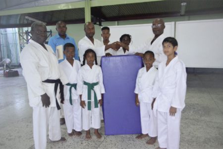Lennox Brummell (third left) hands over one of the mats to Sensei Winston Dunbar in the presence of members of the  GWRKA.
