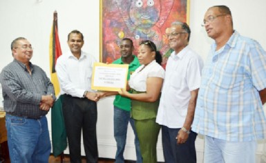 Secretary of the GRFU, Nicole Nero receiving the $1M cheque from Minister of Sport, Dr. Frank Anthony on Monday at the Main Street ministry. 
