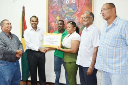 Secretary of the GRFU, Nicole Nero receiving the $1M cheque from Minister of Sport, Dr. Frank Anthony on Monday at the Main Street ministry.