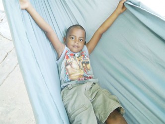 A little boy preparing to take a nap in a hammock