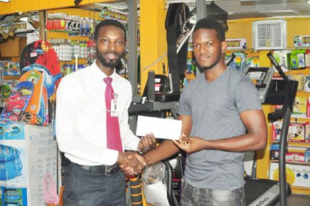 Footballer Kwadro Garnett receives his sponsorship checque from Giftland Officemax Public Relations Manager Compton Babb after being crowned ambassador yesterday. (Orlando Charles photo)
