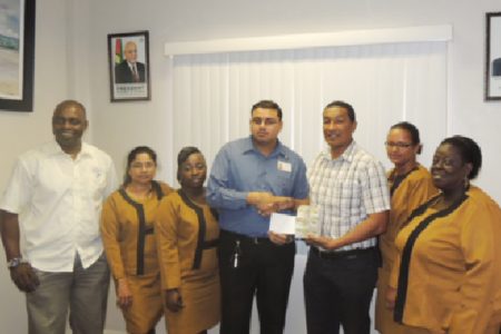 Finance Officer, Latchman Kumar hands over a cheque to co-founder of the K&S Organization, Kashif Muhammad while in the presence of fellow employees and Aubrey ‘Shanghai’ Major.