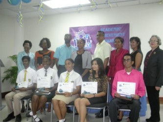 Seated from left are the awardees: Cecil Cox, Jubilante Cutting, Akeila Wiltshire, Reshma Ramdahin and Akash Jairam. Flanking the children’s parents are: Denise Hobbs, General Manager, Corporate and Management Services (left) and Patricia Plummer, General Manager, Credit (right).