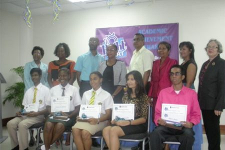 Seated from left are the awardees: Cecil Cox, Jubilante Cutting, Akeila Wiltshire, Reshma Ramdahin and Akash Jairam. Flanking the children’s parents are: Denise Hobbs, General Manager, Corporate and Management Services (left) and Patricia Plummer, General Manager, Credit (right).