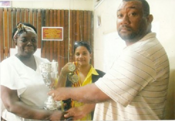 RHTYSC Secretary/CEO Hilbert Foster (right) presents a number of medals to New Amsterdam School Deputy Head Teacher Shondell Phillips (left) for its annual graduation ceremony as another staff member looks on. 