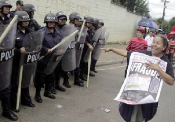 A supporter of Xiomara Castro, presidential candidate of the Liberty and Refoundation party (LIBRE), laughs and points as she holds up a poster with the word ‘’Fraud’’ written on it, as she demonstrates next to riot police officers standing guard during a protest against the results of the presidential election in Tegucigalpa December 1, 2013. (Reuters/Jorge Cabrera)