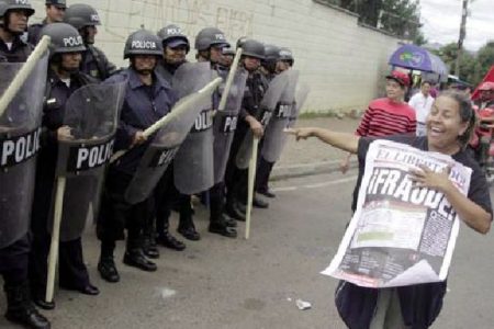 A supporter of Xiomara Castro, presidential candidate of the Liberty and Refoundation party (LIBRE), laughs and points as she holds up a poster with the word ‘’Fraud’’ written on it, as she demonstrates next to riot police officers standing guard during a protest against the results of the presidential election in Tegucigalpa December 1, 2013. (Reuters/Jorge Cabrera)