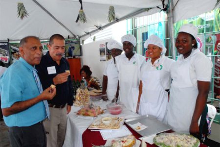 Modest token: Agriculture Minister Dr Leslie Ramsammy (left) has a taste of one of the pineapple goodies placed on display at the corner of Robb and Alexander streets last Friday