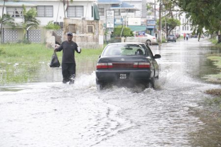Just making sure his food doesn’t get wet: A pedestrian struggles through nearly knee-high water along Carmichael Street yesterday, holding his drink and food aloft as a car splashes by. Sections of the city were once again flooded yesterday after heavy rainfall. (Photo by Arian Browne)