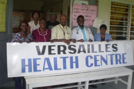 Versailles sign: Resident of Versailles and local businessman Max Massiah, in collaboration with Eureka Medical Laboratory, yesterday presented the Versailles Health Centre with a sign valued $30,000. The Health Centre, which was established last year, had been functioning without a sign since its development. The centre is currently in need of a “bush cutter” machine to maintain its surroundings. In photo: Max Massiah (centre) stands surrounded by staff members of the health centre and residents of Versailles. 