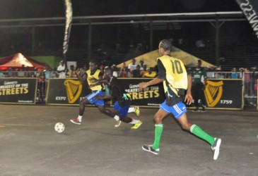 Leon Fredericks (left/yellow vest) of Queen Street Tiger Bay battling with Stevedore Housing Scheme’s Steven Dolphin (centre/black vest) for possession of the ball while team mate Deon Alfred (No.10) looks on. (Orlando Charles photo)