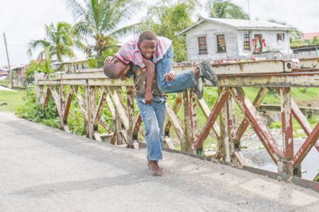 He ain’t heavy… Boy captured fetching his friend across a bridge along the Railway Embankment at Buxton, East Coast Demerara yesterday. (Photo by Arian Browne)