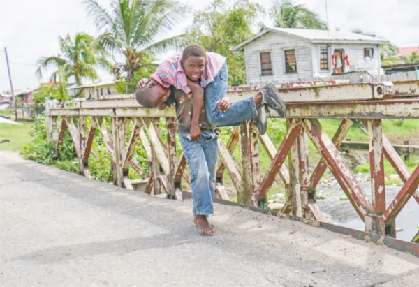 He ain’t heavy… Boy captured fetching his friend across a bridge along the Railway Embankment at Buxton, East Coast Demerara yesterday. (Photo by Arian Browne)   