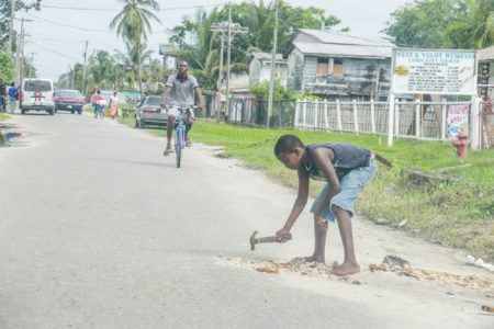 Boy with the hammer! A young boy filling potholes along Front Road, West Ruimveldt, Georgetown (Photo by Arian Browne)