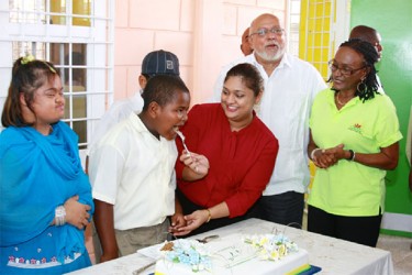 Education Minister Priya Manickchand sticks the PRRC’s 47th anniversary cake with one of its students while President Donald Ramotar, Rehabilitation Officer Cynthia Massay and students look on.  