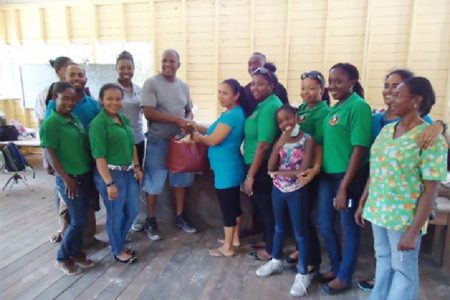 The Rotary Club of Demerara presents a donation of clothing to the head teacher at the school in Malali during a medical outreach, while Rotarians and Rotaractors look on.
