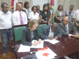 Canadian High Commissioner Nicole Giles (left) and Clerk of the National Assembly Clerk Sherlock Isaacs (centre) sign the MoU as Speaker of the House Raphael Trotman (right) and other staff look on 