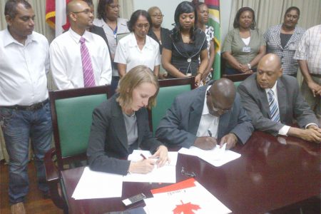 Canadian High Commissioner Nicole Giles (left) and Clerk of the National Assembly Clerk Sherlock Isaacs (centre) sign the MoU as Speaker of the House Raphael Trotman (right) and other staff look on 