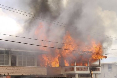 The Grove, East Bank Demerara home of Vanessa Higgins engulfed in flames yesterday. At left is Kavita Lall’s home which was damaged but saved. 