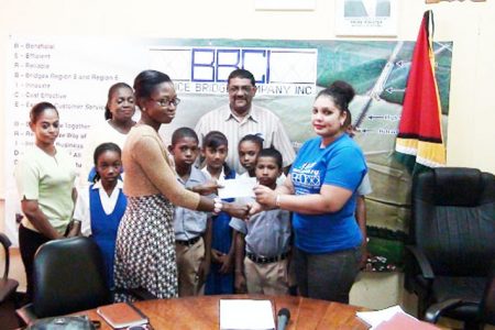 BBCI Administrative Assistant Bibi F Alli (right) presents a sponsorship cheque to a Region Six Regional Mashramani Committee member for the Spelling Bee competition while a number of children and officials look on