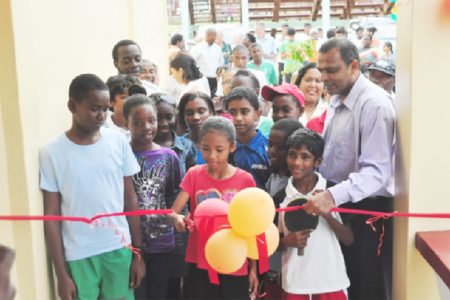 Minister of Sport, Dr. Frank Anthony watches on as a young sportswoman symbolically cuts the ribbon to open the National Resource Centre. (Orlando Charles photo)