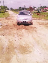 A car navigating through a section of the road which was patched up by residents with mud.  