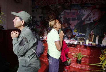 A military woman and a local resident pray at the “Saint Hugo Chavez” altar at the 23 de Enero neighbourhood in Caracas March 5, 2014. REUTERS/Tomas Bravo