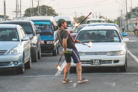 Stop light entertainment: Persons waiting for traffic lights at the corner of Mandela Avenue and the East Bank Demerara Highway yesterday were entertained by a man juggling fire sticks. Many seemed pleased at the distraction. (Photo by Arian Browne)