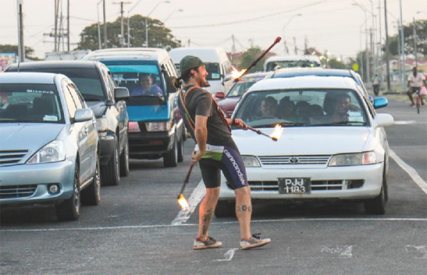 Stop light entertainment: Persons waiting for traffic lights at the corner of Mandela Avenue and the East Bank Demerara Highway yesterday were entertained by a man juggling fire sticks. Many seemed pleased at the distraction. (Photo by Arian Browne)
