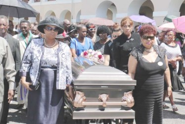 The casket with the remains of former APNU MP and Attorney at Law Deborah Backer being escorted yesterday afternoon  by APNU MPs Amna Ally (right) and Volda Lawrence from Public Buildings where a ceremony was held. (Arian Browne photo) 