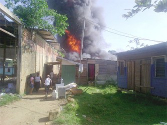 Residents removing items from buildings as the fire rages in the background. A fuel boat exploded at Turn Basin yesterday and in the aftermath that vessel along with four other boats and five buildings were burnt.