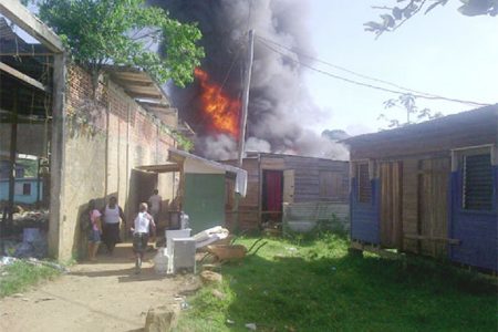 Residents removing items from buildings as the fire rages in the background. A fuel boat exploded at Turn Basin yesterday and in the aftermath that vessel along with four other boats and five buildings were burnt.