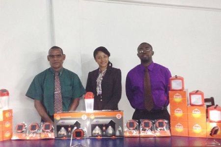 (L to R) Christopher Jacques, Chief Operations Officer, Holly Persaud, Public Relations Consultant and Dale Browne, Chief Executive Officer, all of Rehoboth Group, pose with a display of D.Light solar energy products.