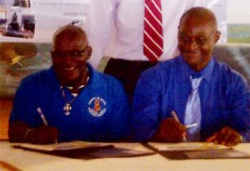 Uriel Dey (left) symbolically signing the declaration on behalf of New Amsterdam Mayor, Claude Henry. At right is Orrin Gordon, Chairperson, IMC Linden. 