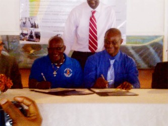 Uriel Dey (left) symbolically signing the declaration on behalf of New Amsterdam Mayor, Claude Henry. At right is Orrin Gordon, Chairperson, IMC Linden. 