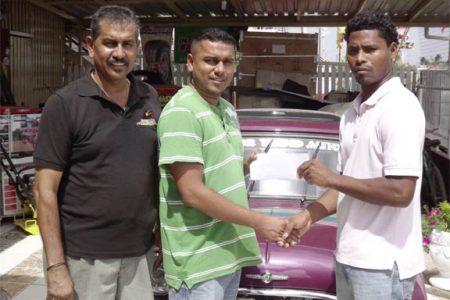 Benedict Prince (right) collects the cheque from Kevin Deodass of Motor Trend Auto in presence of the manager Jailall Deodass.
