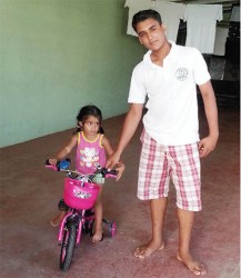 Little Sariah Persaud riding her bike with Stefan Harinauth watching out for her