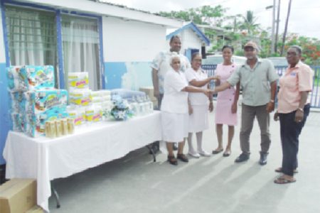 
Food for the Poor (Guyana) Inc donated a number of items to the Chest Clinic of the Georgetown Public Hospital Corporation recently. Nurse in charge of the clinic, Sursattie Rajcumar said that the charity has been donating items to the clinic for about five years, according to a press release. The items are very useful to the nurses and to the patients, she said, and commended the organisation for its continuous support to the health sector. The charity’s PR Manager, Wayne Hamilton, said it is cognisant of the needs of the health sector and the difficult conditions that nurses operate under daily, and pledged to lend support whenever possible to the hospital. In picture: Hamilton (second from right) shares a handshake with Rajcumar while other representatives look on.  The items are displayed on a table at left. 