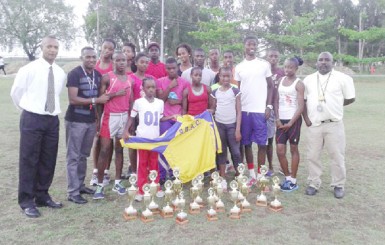 Athletes of the Running Brave Athletic Club pose with the hardware they earned at the recently concluded Hampton Games. They are flanked by coaches, Sham Johnny and Julian Edmonds along with president of the club and the AAG, Aubrey Hutson. 