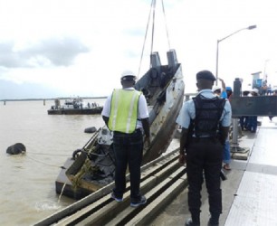 A police officer and DHB staff look on as the tug is pulled out of the river yesterday. (Photo by Aneka Edwards/Ministry of Public Works) 