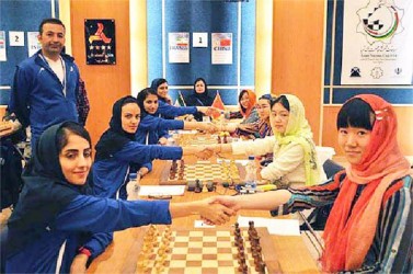 Iran A and China observe the traditional collective handshake before the beginning of their team encounter at the Women’s 2014 Asian Nations Chess Cup in Tabriz, Iran. The championship tournament ended on Friday. The Chinese team is FIDE higher ranked than the Iranians and thereby defeated their opponents, but only after their Board Four capitulated, thus giving the Chinese victory. The three top Iranian boards had held the powerhouse Chinese team to tame draws. In the photograph, the Chinese [right] are wearing similar headdresses much to the delight of their hosts, which one commentator considered “a very kind act.’’   