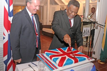 Prime Minister Sam Hinds cutting the cake at the reception last night in honour of the birthday of Queen Elizabeth II. At left is British High Commissioner Andrew Ayre. (Arian Browne photo)
