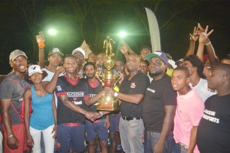 West Front Road captain Hubert Pedro (black vest) collecting the championship trophy from Mackeson Brand Manager Jamal Douglas while members of the team and spectators look on.