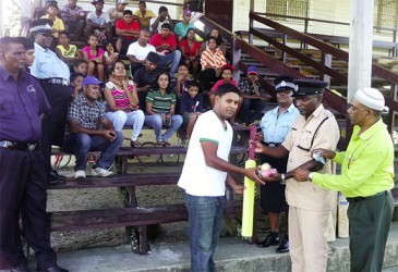 Assistant Superintendent, Joshua Harvey-John hands over some of the cricket gear to Naipaul Molaha in the presence of other officers and group members     