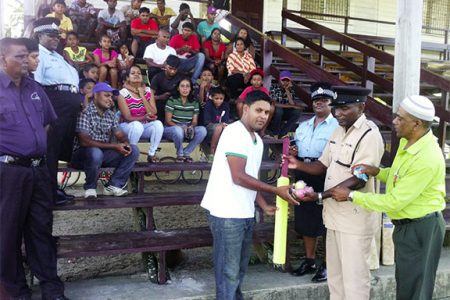 Assistant Superintendent, Joshua Harvey-John hands over some of the cricket gear to Naipaul Molaha in the presence of other officers and group members  
 